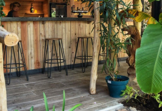 Bar in legno accogliente con sgabelli, lampade e piante al campeggio Les 3 Cantons in Occitania, Francia.