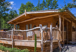 Wooden cabin at Campsite Les 3 Cantons, Occitanie, France, surrounded by lush trees and sunny weather.