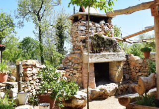 Stone fireplace and garden at Campsite Les 3 Cantons in Occitanie, France, surrounded by plants and wood.
