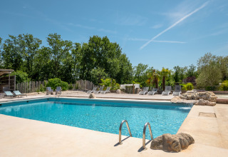 Outdoor swimming pool with sun loungers and trees at Campsite Les 3 Cantons in Occitanie, France, on a sunny day.