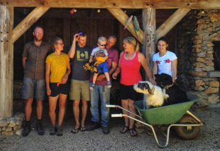 Group photo with six adults, a child, and two dogs in a wheelbarrow at Campsite Les 3 Cantons, Occitanie, France.