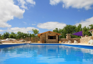Swimming pool with a stone building and trees in the background at Campsite Les 3 Cantons, Occitanie, France.