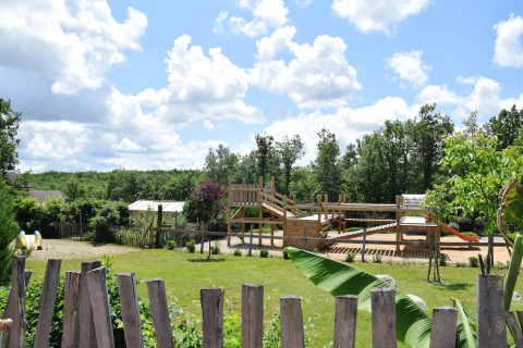 Children's playground and grassy area at Campsite Les 3 Cantons in Occitanie, France, on a sunny day.