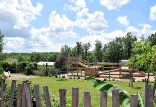 Children's playground and grassy area at Campsite Les 3 Cantons in Occitanie, France, on a sunny day.