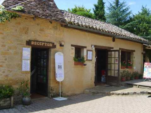 Edificio della reception al campeggio La Grande Véyière in Nouvelle-Aquitaine, Francia, con fiori e cartelli.