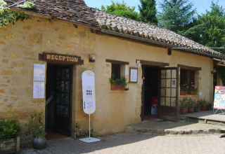 Edificio della reception al campeggio La Grande Véyière in Nouvelle-Aquitaine, Francia, con fiori e cartelli.