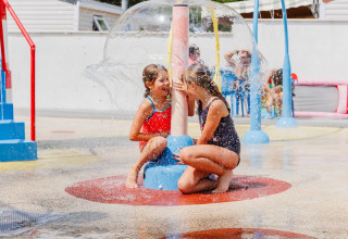 Two children in swimsuits play under a water fountain at Flower Camping l'Escale du Perthuis holiday park.