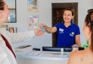 Receptioniste overhandigt sleutel aan gasten bij Flower Camping l'Escale du Perthuis in Pays de la Loire, Frankrijk.