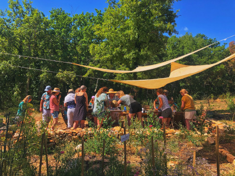 Group of people gather under sun shades at a table in a garden at Les 3 Cantons, Occitanie, France.