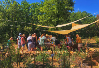 Gruppo di persone riunite sotto teli ombreggianti in un giardino a Les 3 Cantons, Occitania, Francia.