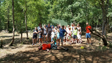 Group of children and adults at Campsite Les 3 Cantons in Occitanie, France, standing in a sunny forest area.