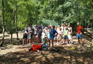 Group of children and adults at Campsite Les 3 Cantons in Occitanie, France, standing in a sunny forest area.