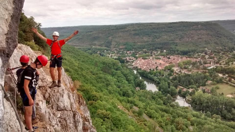 Tre persone arrampicano sulle rocce al campeggio Les 3 Cantons con vista su valle boscosa e villaggio in Occitania.