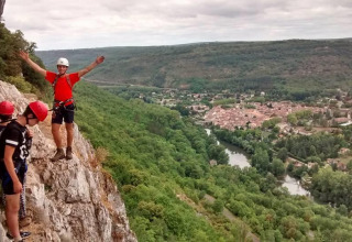 Tre persone arrampicano sulle rocce al campeggio Les 3 Cantons con vista su valle boscosa e villaggio in Occitania.