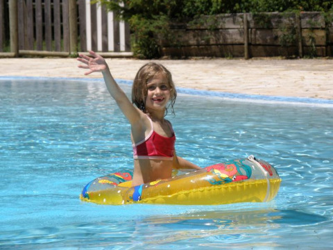 Bambina in bikini rosso sorride e saluta in un salvagente colorato nella piscina del campeggio La Grande Véyière, Francia.