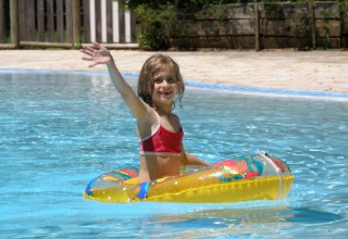 Bambina in bikini rosso sorride e saluta in un salvagente colorato nella piscina del campeggio La Grande Véyière, Francia.