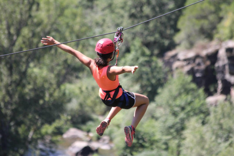 Person ziplining with a red helmet at Campsite «Les 3 Cantons» in Occitanie, France, surrounded by greenery.