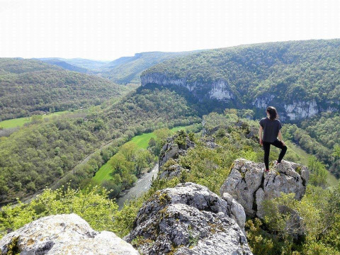 Person stands on a rocky outcrop overlooking a lush valley at Campsite Les 3 Cantons in Occitanie, France.