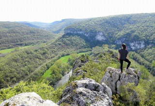 Person stands on a rocky outcrop overlooking a lush valley at Campsite Les 3 Cantons in Occitanie, France.