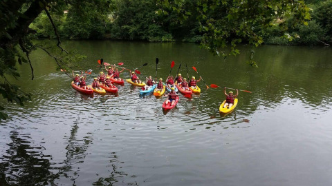 A group kayaking on a scenic river near St Antonin Noble Val, Occitanie, France, surrounded by lush greenery.