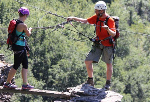 Two people cross a rope bridge with safety gear at Campsite Les 3 Cantons, Occitanie, France.