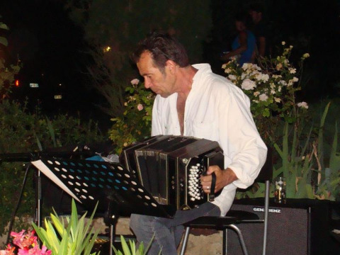 Uomo che suona il bandoneón all'aperto al campeggio La Grande Véyière in Nouvelle-Aquitaine, Francia, di sera.