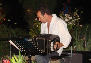 Uomo che suona il bandoneón all'aperto al campeggio La Grande Véyière in Nouvelle-Aquitaine, Francia, di sera.