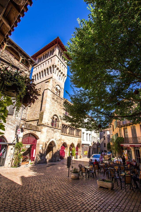 Photo of a cobbled square with café seating and a medieval tower at Les 3 Cantons campsite in Occitanie, France.