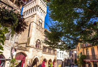 Piazza lastricata con tavolini da caffè e torre medievale al campeggio Les 3 Cantons in Occitania, Francia.