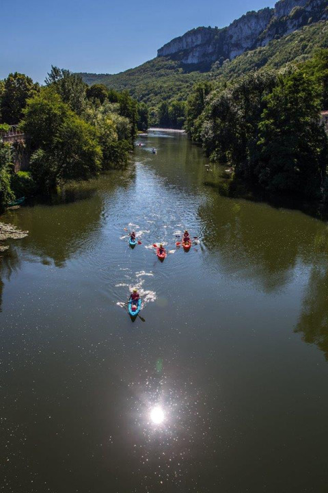People kayak down a scenic river with forested banks at Campsite «Les 3 Cantons» in Occitanie, France.