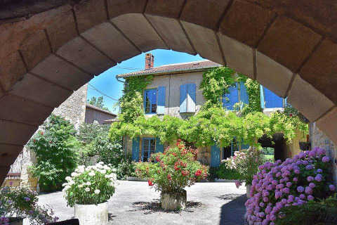 Casa in pietra con persiane blu e fiori vivaci al campeggio Les 3 Cantons in Occitania, Francia.