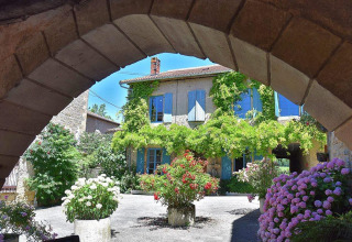Charming stone house with blue shutters and vibrant flowers at Campsite Les 3 Cantons in Occitanie, France.