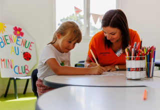 Girl and adult coloring together at a table in the kids’ club at Flower Camping l'Escale du Perthuis, France.