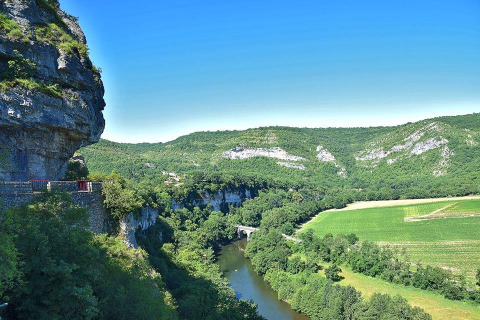 Scenic view of cliffs, river, and green fields at Campsite «Les 3 Cantons» in Occitanie, France on a sunny day.