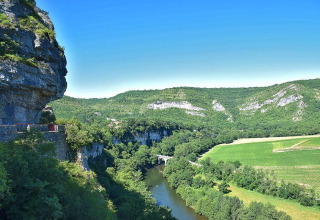 Scenic view of cliffs, river, and green fields at Campsite «Les 3 Cantons» in Occitanie, France on a sunny day.