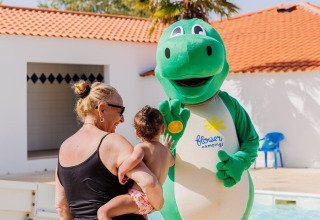 Una donna e un bambino incontrano la mascotte dinosauro verde al Flower Camping l'Escale du Perthuis in Francia.