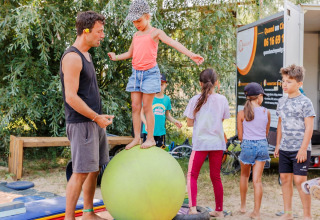 Niños juegan y se equilibran sobre una gran pelota en Flower Camping l'Escale du Perthuis, Pays de la Loire, Francia.