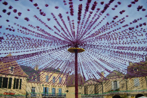 Festone viola decorano una piazza circondata da case di pietra a Molières, Nouvelle-Aquitaine, Francia.