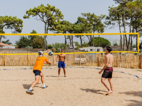 Tre mænd spiller beachvolleyball på sandet under solrige forhold i Flower Camping l'Escale du Perthuis, Pays de la Loire.