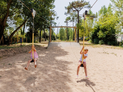 Dos niños juegan en una tirolina en un parque infantil de arena en Flower Camping l'Escale du Perthuis, Francia.