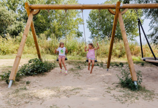 Due bambini si dondolano su un'altalena in un parco giochi sabbioso al Flower Camping l'Escale du Perthuis, Pays de la Loire.