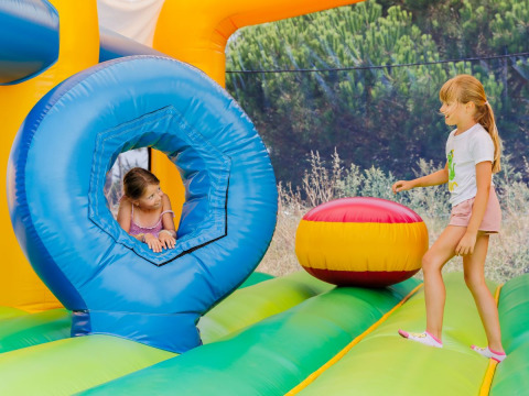 Due bambine giocano su un castello gonfiabile colorato in un parco vacanze con glamping tra la natura.