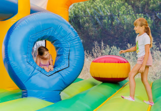 Deux enfants jouent sur un château gonflable coloré dans un parc de vacances avec glamping, entourés d’arbres.