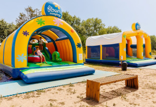 Twee kleurrijke springkastelen en een houten bank bij Flower Camping l'Escale du Perthuis in Pays de la Loire, Frankrijk.