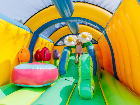 Enfant jouant sur un château gonflable coloré dans un parc de vacances offrant des hébergements glamping.