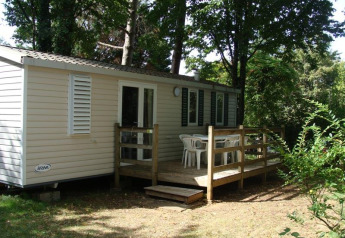 Mobil-home Comfort au camping La Grande Véyière en France, entouré d’arbres avec terrasse en bois.