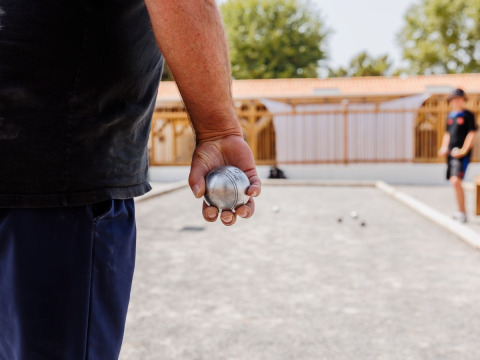 Iemand houdt een petanque-bal vast om te spelen op het veld bij Flower Camping l'Escale du Perthuis.