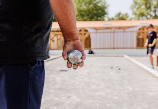A person holds a pétanque ball ready to play on a court at Flower Camping l'Escale du Perthuis, France.