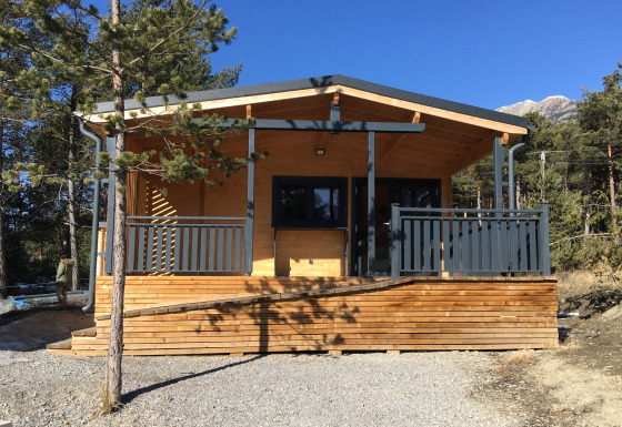 Houten chalet met airconditioning, omgeven door dennen en bergen, zonnige dag bij de lodge.