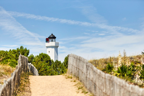 Camino de arena con valla de madera hacia un faro junto a árboles, cerca de La Tranche-sur-Mer, Pays de la Loire, Francia.